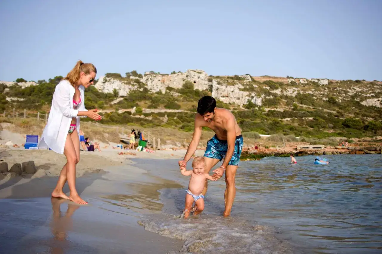 Famiglia felice a Minorca con bambini che imparano a camminare in mare.