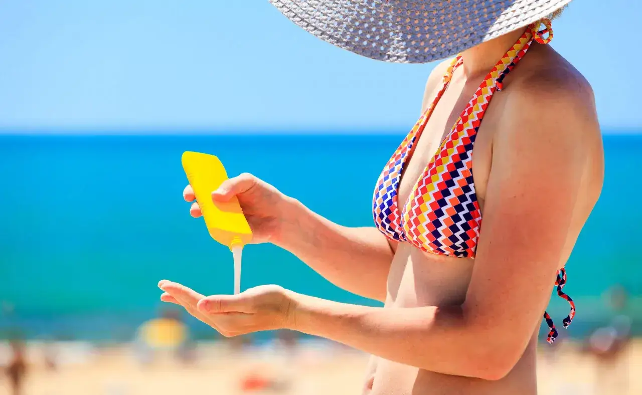 Donna in bikini applica crema solare con protezione 20. Il mare azzurro fa da sfondo.