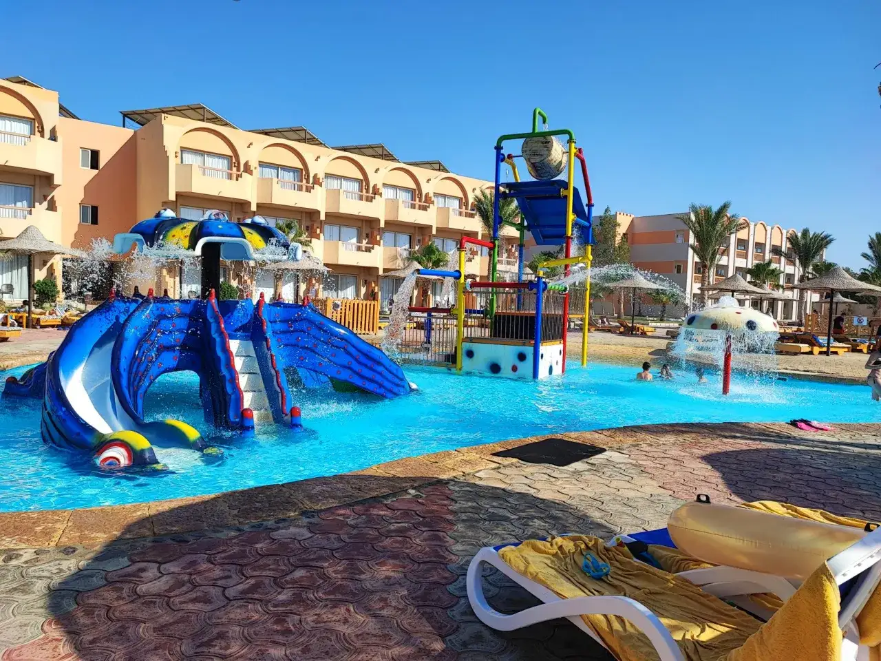 Divertimento acquatico a Marsa Alam con bambini: scivoli blu, giochi d'acqua e un hotel sullo sfondo.
