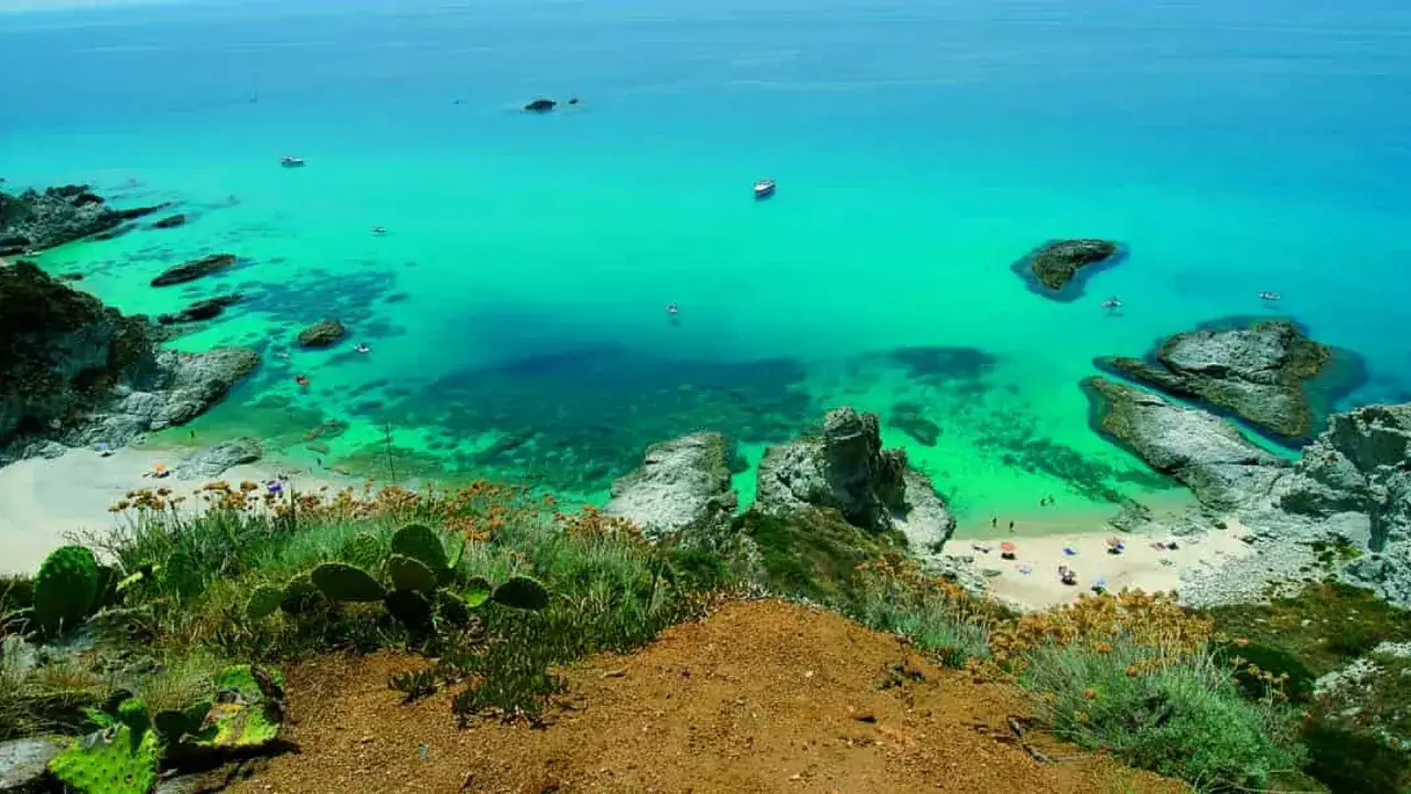 Spiaggia incantevole in Calabria, mare cristallino con scogli e vegetazione mediterranea.
