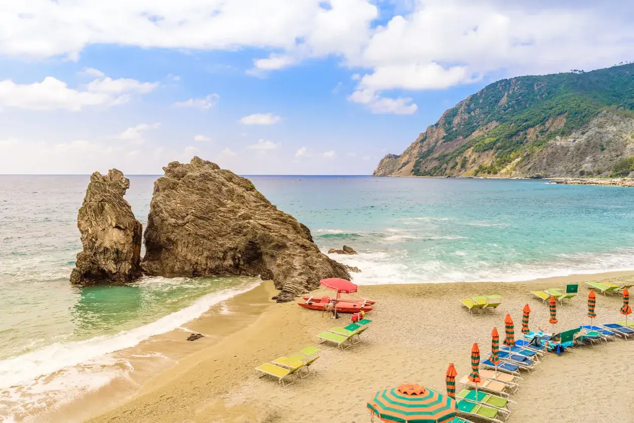 Spiagge sabbia Liguria: scogli imponenti, mare turchese e lettini pronti per godersi il sole.
