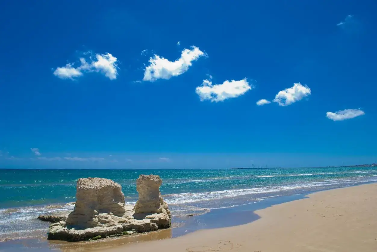 Scogliere calcaree sulla spiaggia dorata, mare azzurro e cielo limpido in Sicilia orientale.