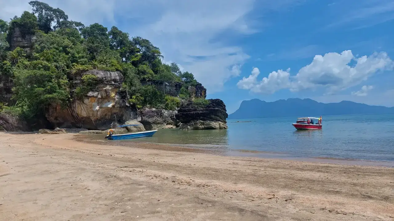 Spiaggia in Malesia con bambini su una barca rossa. Rocce verdi e mare calmo.