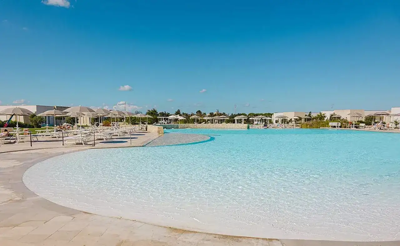 Ampia piscina con acqua cristallina e lettini prendisole sotto ombrelloni al le cesine resort. Cielo azzurro e sole splendente.
