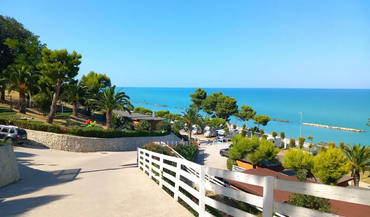 Villaggio Riva Verde Marche: un campeggio con bungalow e camper affacciato sul mare Adriatico, tra palme e pini marittimi.
