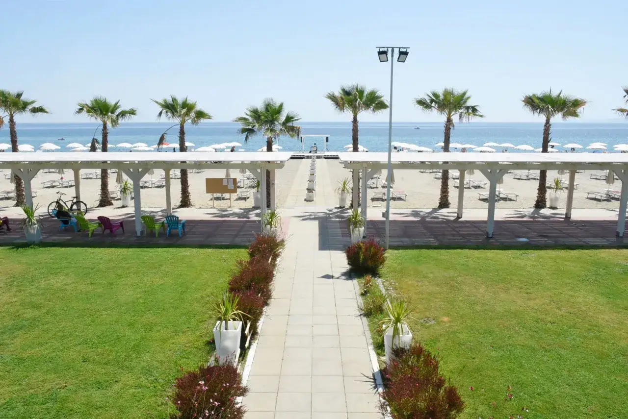 Vacanze al Valtur Calabria Otium Resort: spiaggia attrezzata con lettini, ombrelloni, palme e un percorso che porta al mare azzurro.