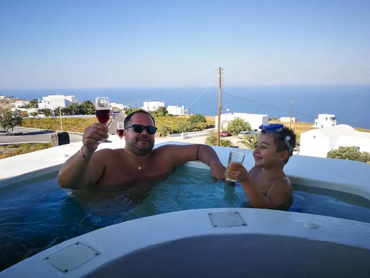 Un uomo e un bambino brindano in una vasca idromassaggio a Santorini, godendosi una vacanza indimenticabile con bambini.