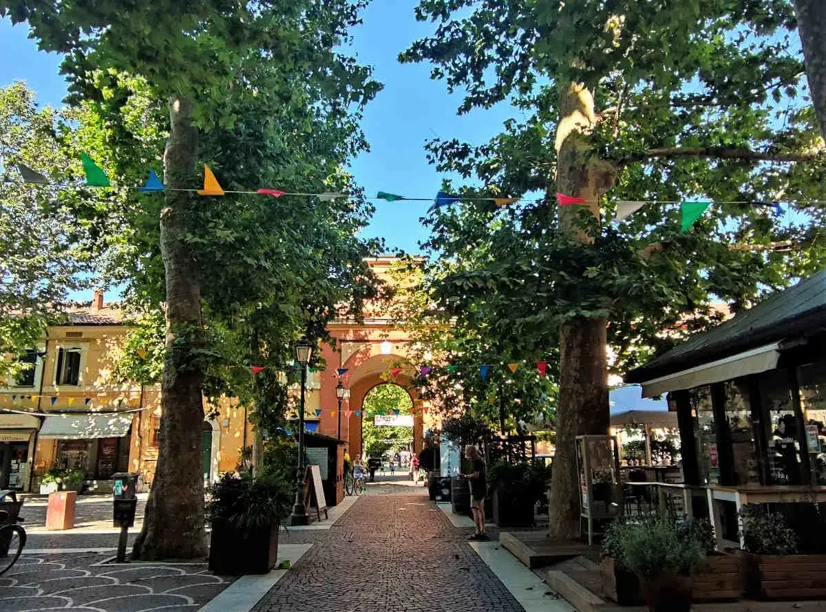 Viale alberato con festoni colorati, ideale per scoprire cosa fare a Cervia. Un arco storico fa da sfondo a questa pittoresca via pedonale.