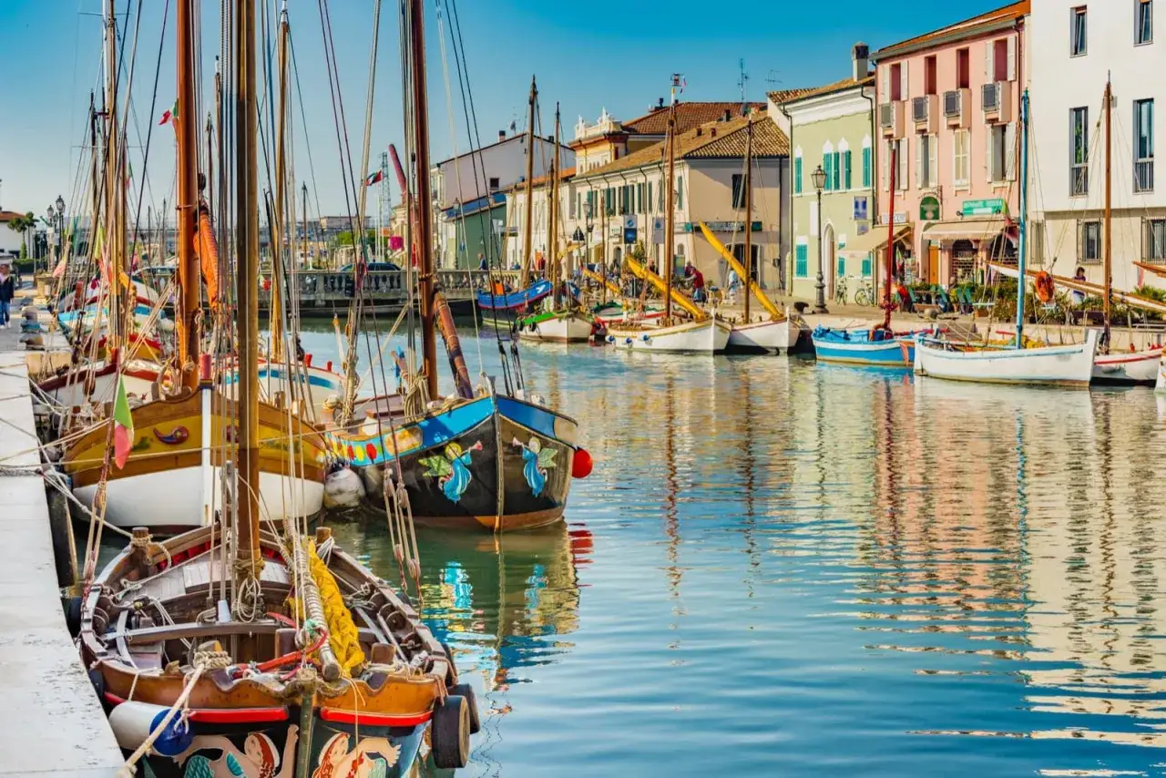 Barche colorate ormeggiate nel canale di Cesenatico, un'ottima idea per cosa fare a Cesenatico, con case vivaci sullo sfondo.