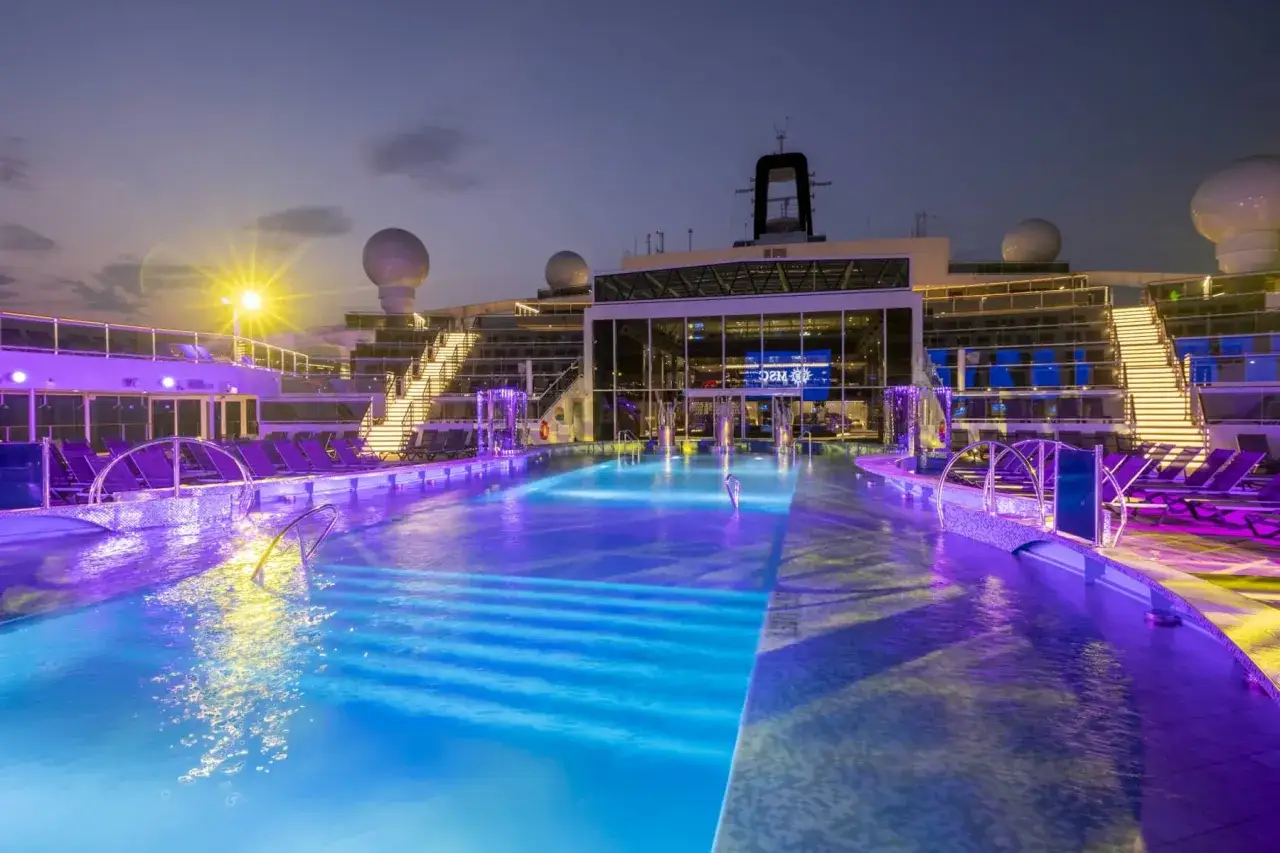 Le piscine illuminate della MSC World Europa creano un'atmosfera magica al tramonto, con luci viola e blu che si riflettono sull'acqua.