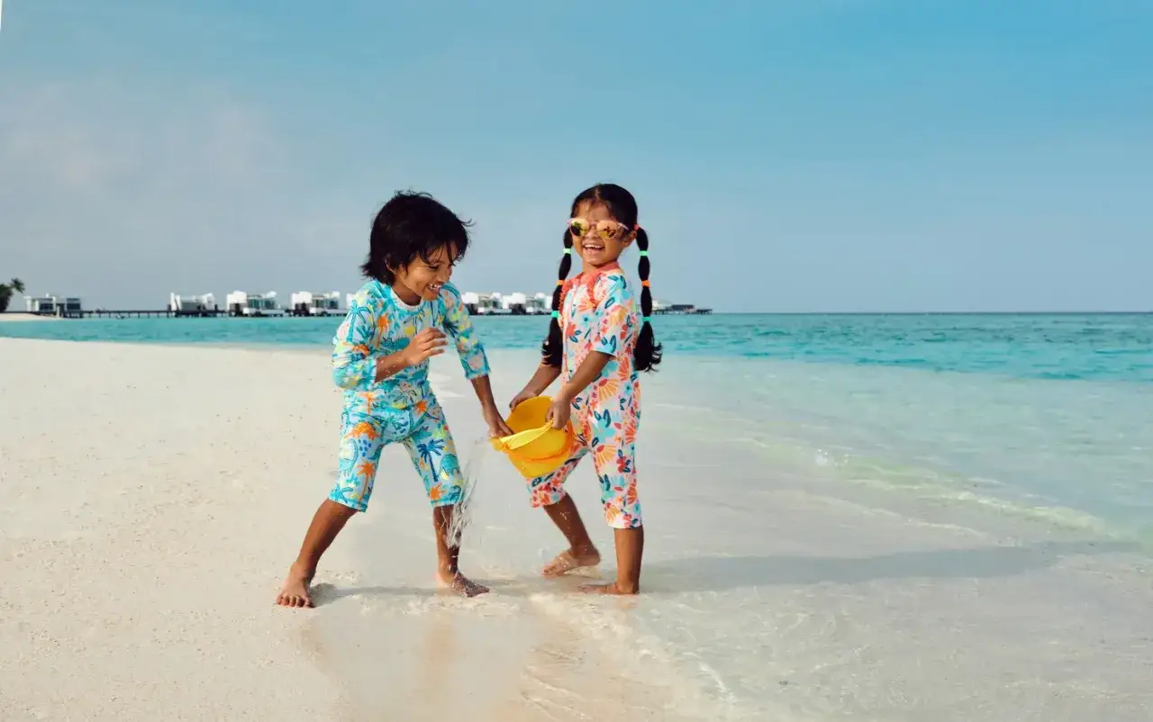 Bambini felici giocano sulla spiaggia delle Maldive con secchiello giallo e costumi colorati.