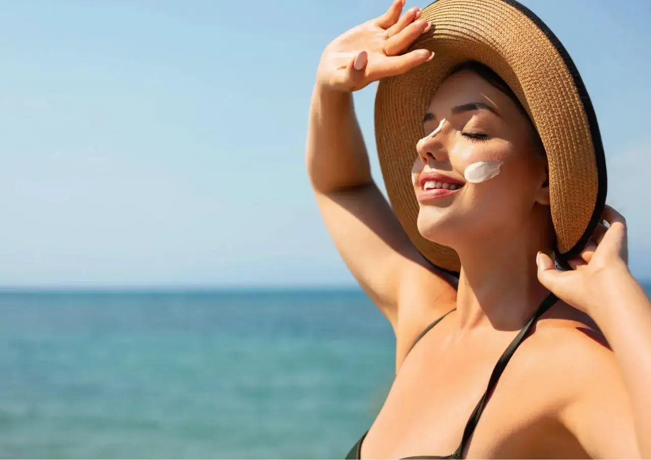 Donna con cappello di paglia e crema solare sul viso, godendosi il mare. La sua pelle non si abbronza, ma è protetta.
