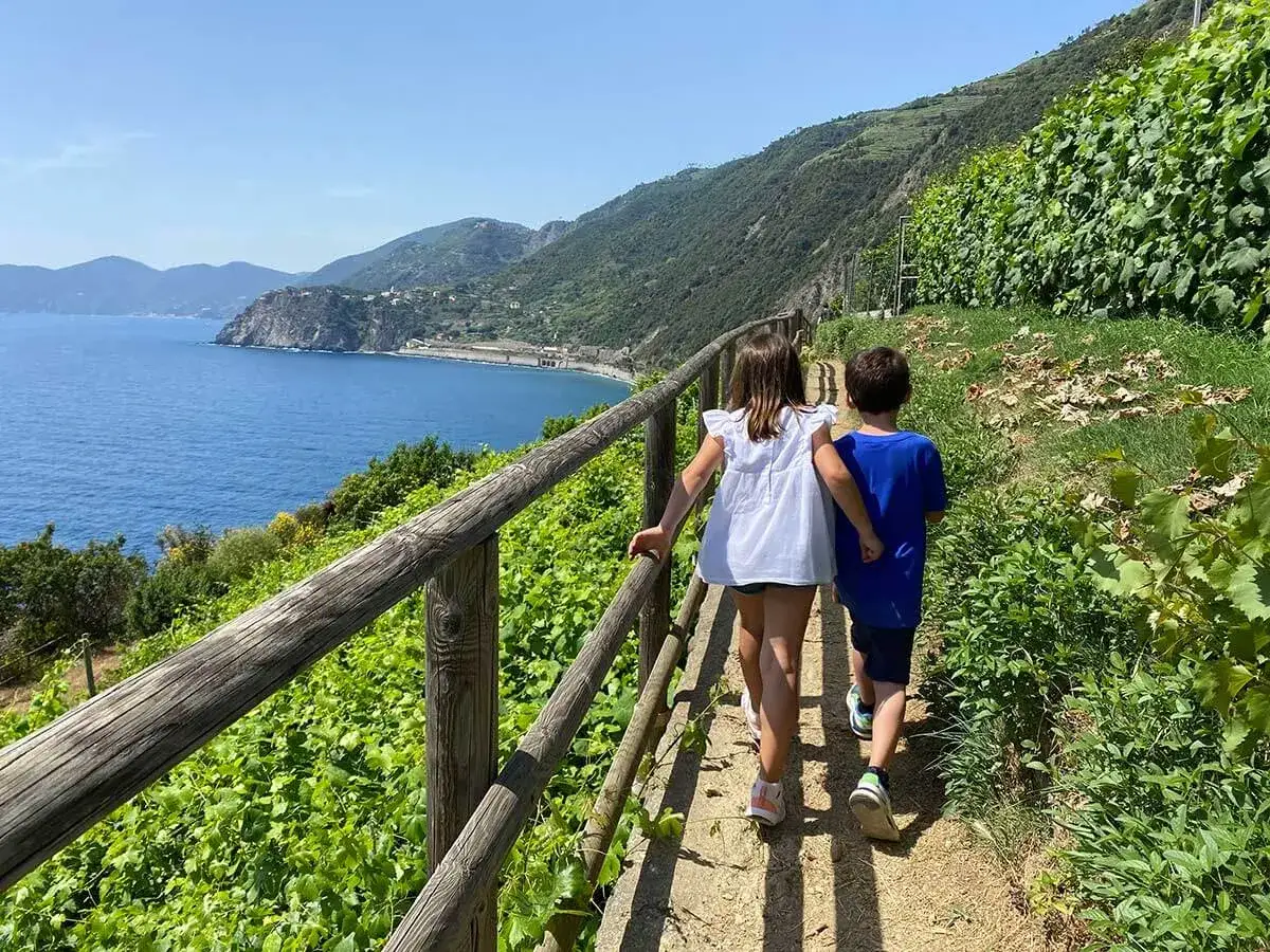 Bambini esplorano i sentieri panoramici delle Cinque Terre, con il mare azzurro e la vegetazione rigogliosa.
