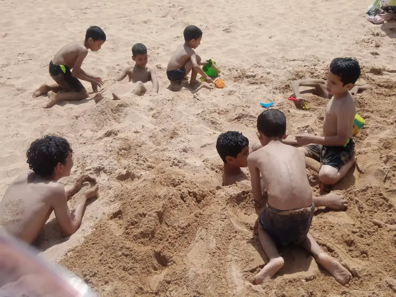 Bambini giocano sulla sabbia in Marocco, alcuni sepolti, altri scavano con palette.