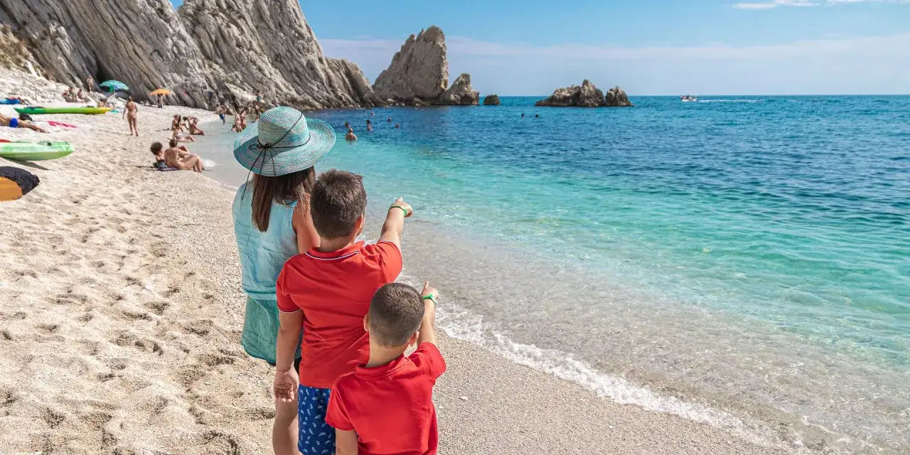 Bambini entusiasti indicano il mare cristallino della Riviera del Conero, con la mamma che li osserva.