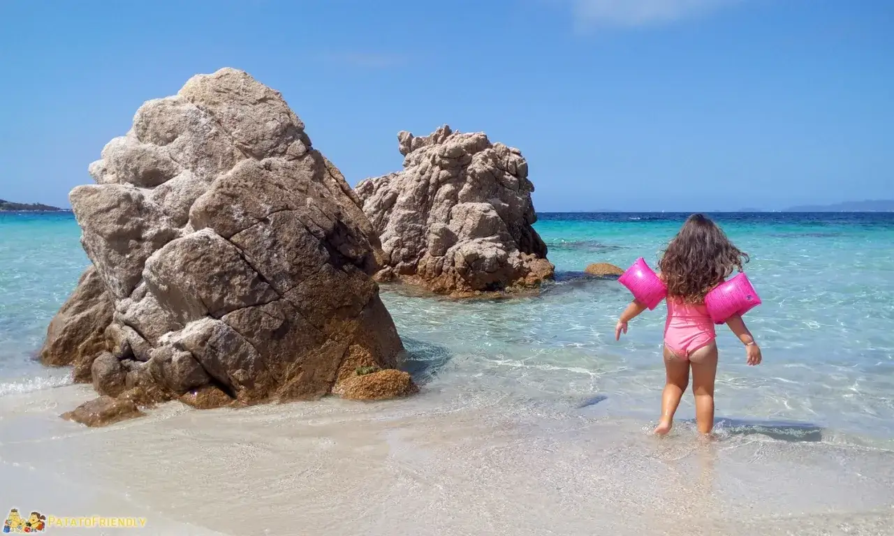 Bambina con braccioli rosa esplora le acque cristalline della Corsica, tra scogli imponenti e sabbia bianca. Vacanze in Corsica con bambini.