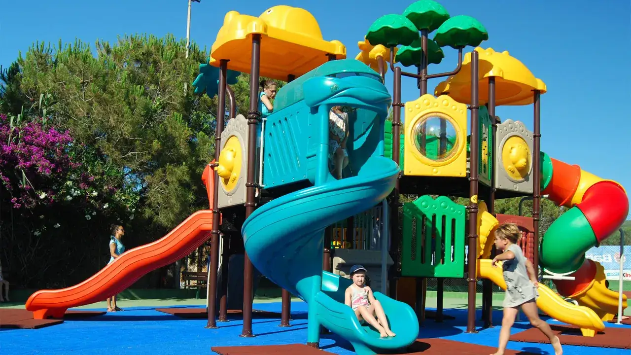 Bambini giocano in un colorato parco giochi, perfetto per i villaggi per famiglie in Sardegna. Divertimento assicurato sotto il sole!