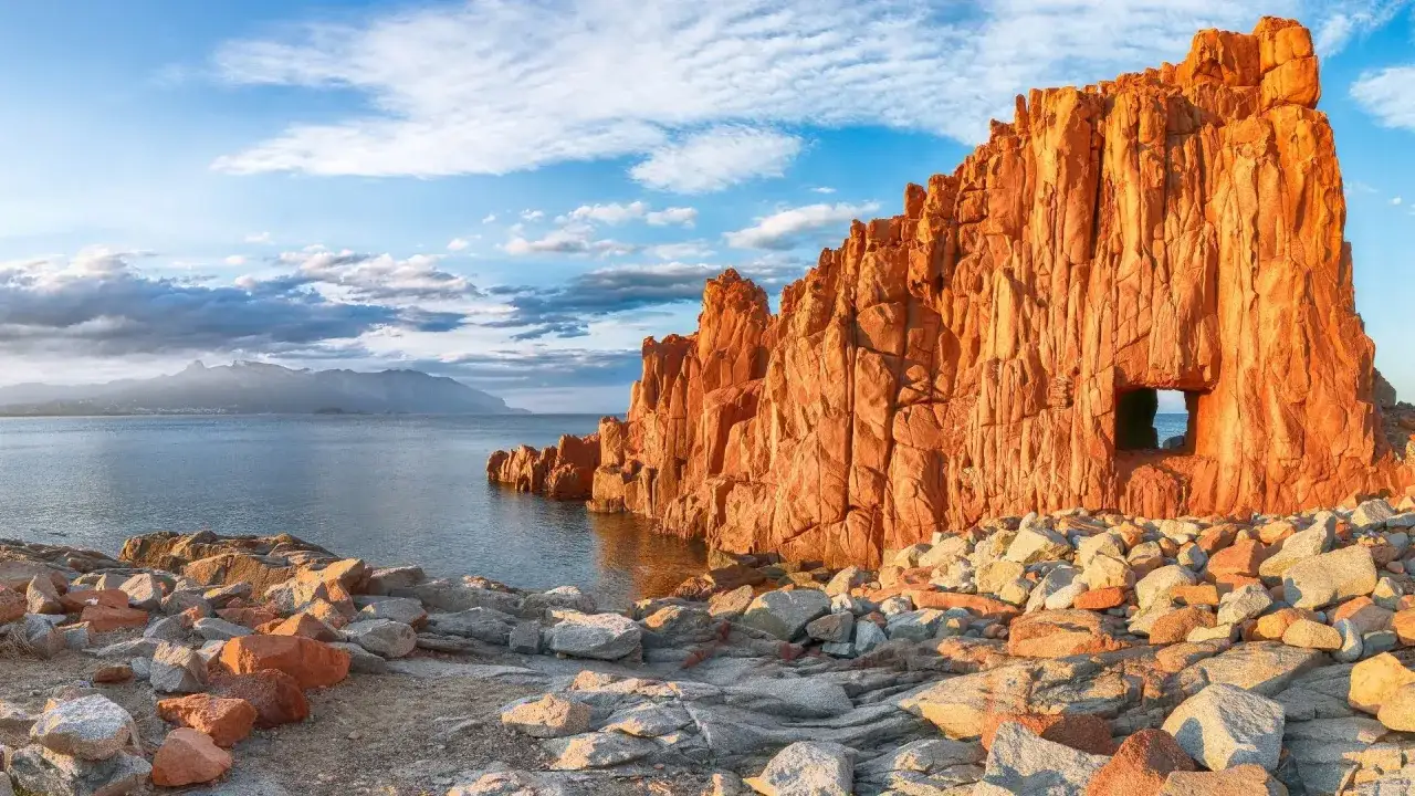 Scogliere rosse a picco sul mare, un'apertura nella roccia ricorda un passaggio segreto verso la spiaggia rosa di Arbatax.