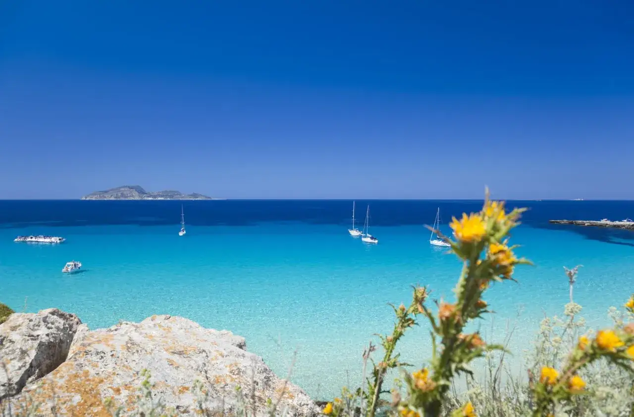 Splendida Sicilia dove andare al mare: acque cristalline, barche a vela e un'isola all'orizzonte.