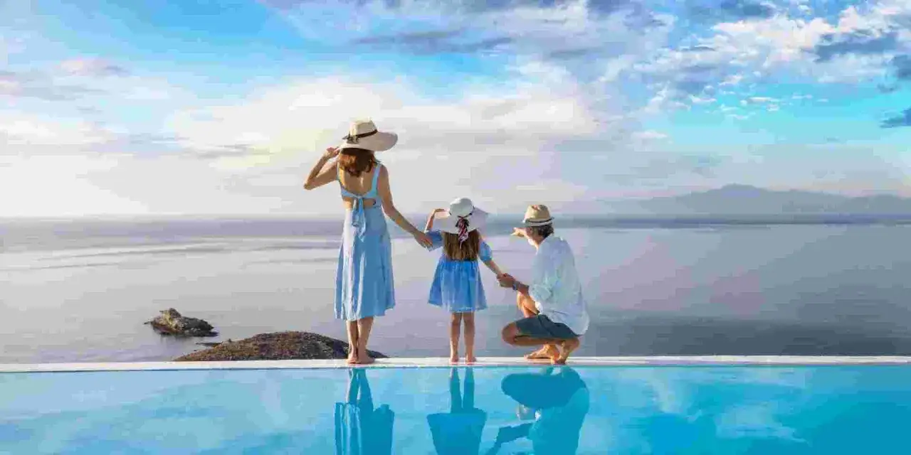 Famiglia felice in vacanza in un Grecia family hotel, con vista sul mare e piscina a sfioro.
