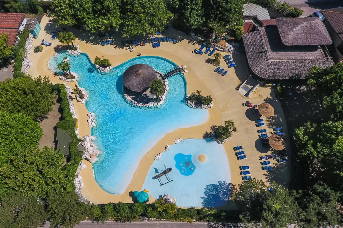 Villaggio vacanze con piscina a forma di laguna, palme e lettini prendisole. Un'oasi tropicale che ricorda il tahiti camping village.