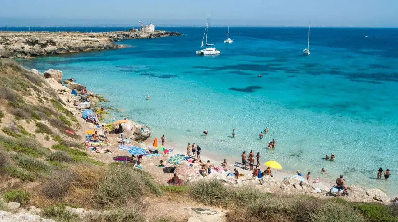 Favignana con bambini: una spiaggia di sabbia e rocce baciata da un mare cristallino, con gente che prende il sole e si gode la vacanza.