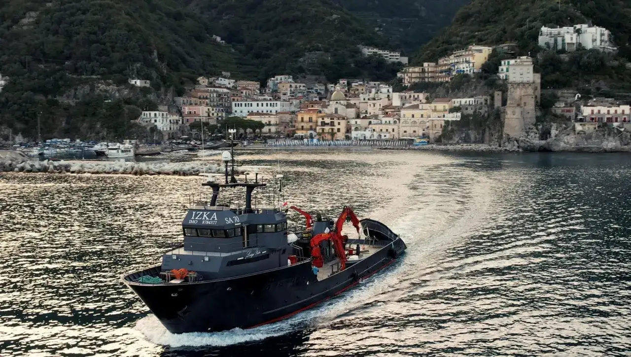 Imbarcazione per la pesca tonno in navigazione, con un pittoresco borgo costiero sullo sfondo.
