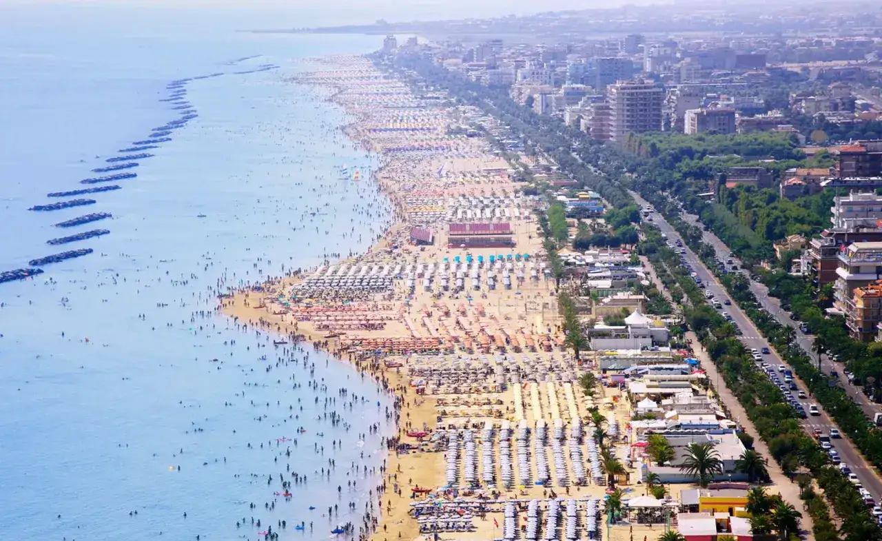 Vista aerea della spiaggia affollata di San Benedetto del Tronto, con ombrelloni, bagnanti e il mare azzurro.