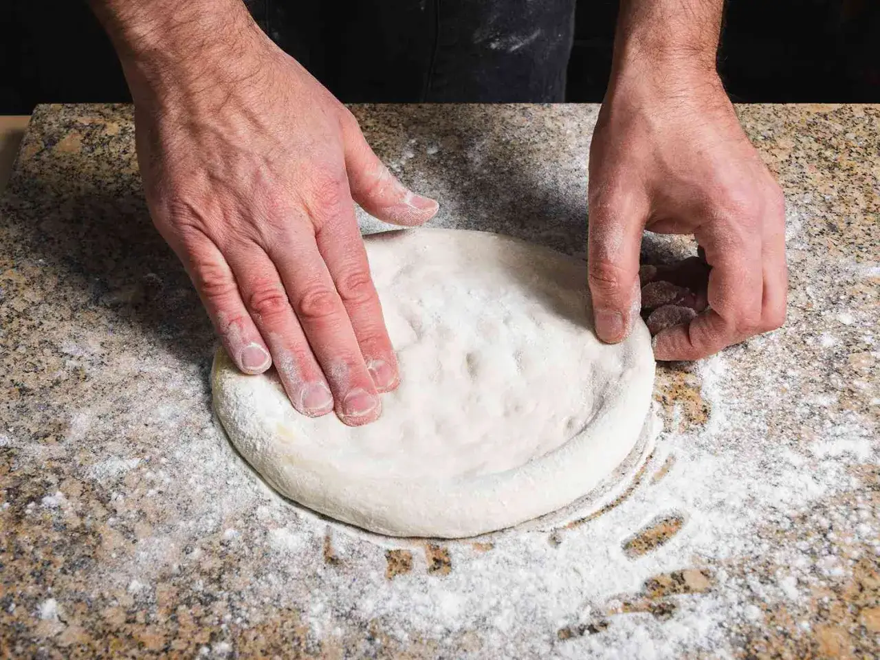 Mani esperte stendono l'impasto per una pizza fatta in casa su un piano di lavoro infarinato.