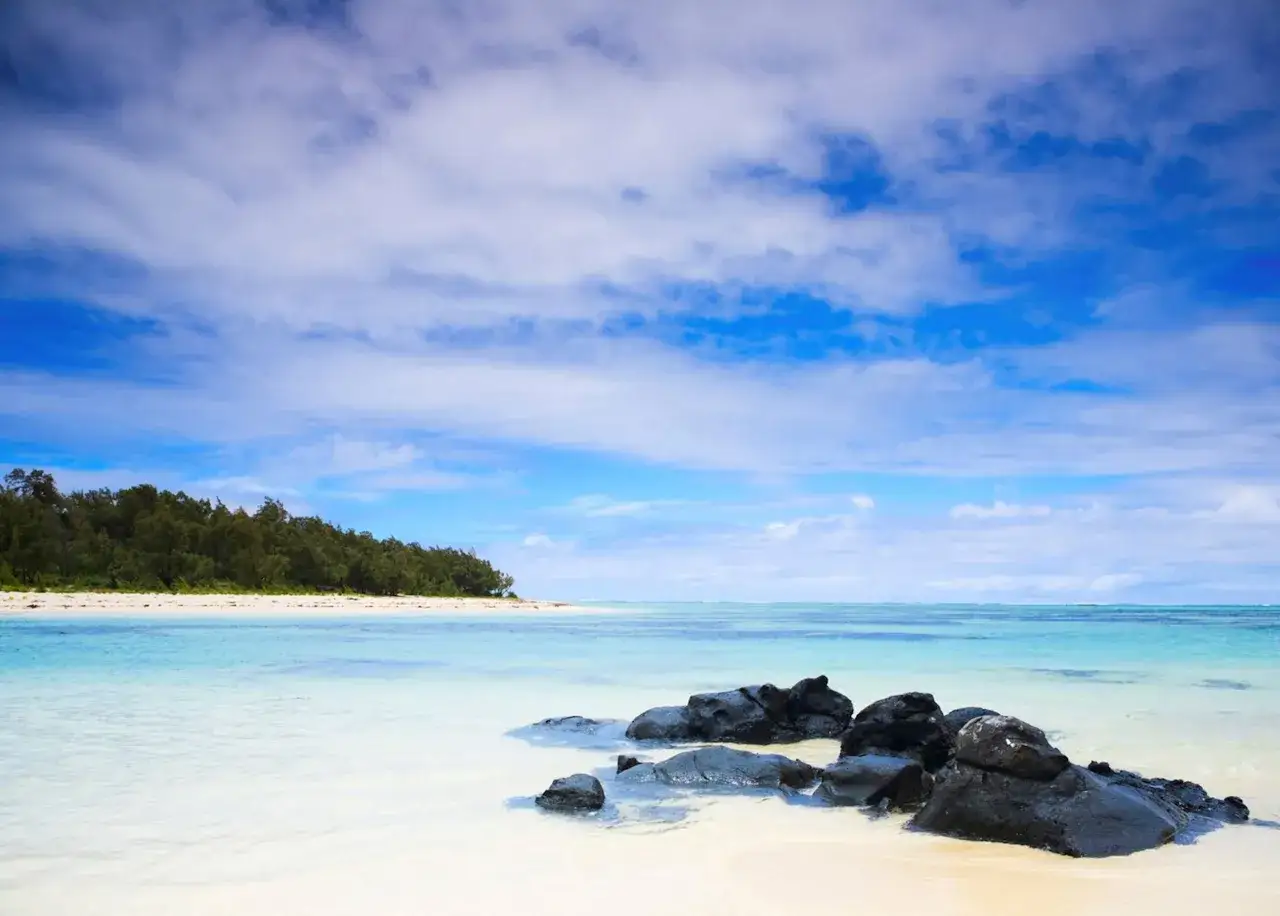 Spiaggia tropicale a Mauritius, con rocce vulcaniche scure sulla riva e una lussureggiante vegetazione sullo sfondo. Ideale per una vacanza a Mauritius con bambini.