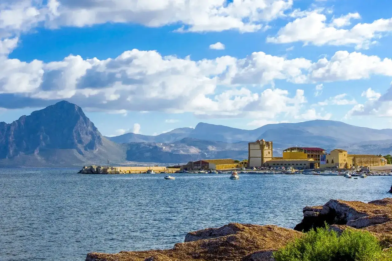 La tonnara di Bonagia, con il suo porto e le montagne sullo sfondo, sotto un cielo azzurro e nuvoloso.