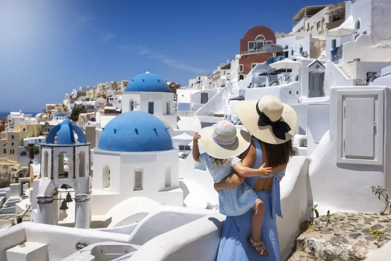 Madre e figlia ammirano le iconiche cupole blu di Santorini, un luogo perfetto per vacanze in famiglia nelle isole greche.