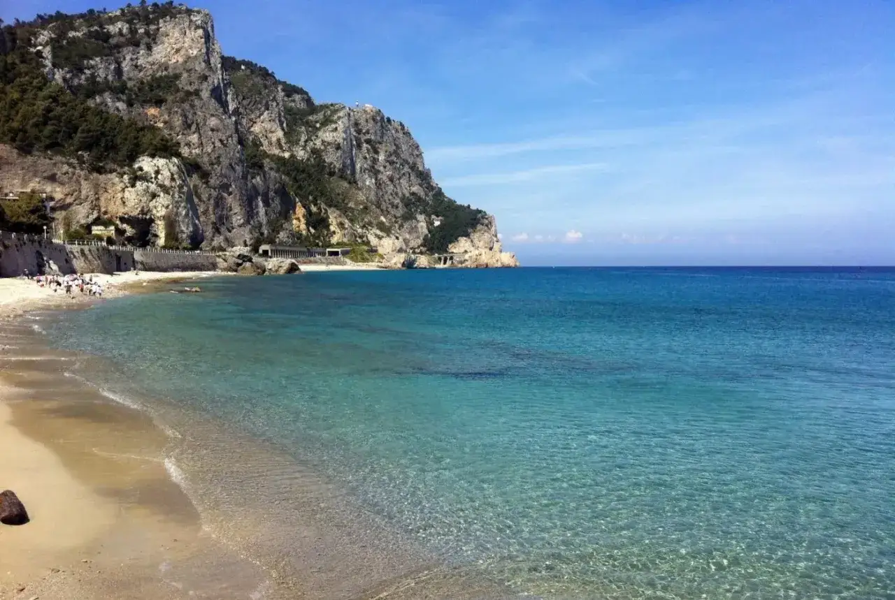 La spiaggia più bella di Varigotti, con acque cristalline che lambiscono la sabbia dorata e imponenti scogliere verdi.