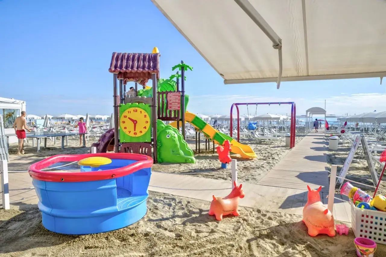 Area giochi per bambini sulla spiaggia, perfetta per le vacanze famiglia mare. Scivoli, altalene e giochi colorati sulla sabbia dorata.