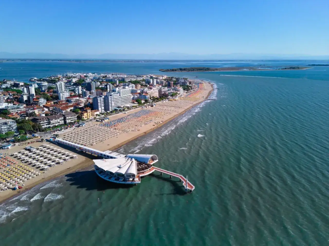 Un'ampia spiaggia attrezzata con ombrelloni colorati e un moderno pontile sul mare del Friuli Venezia Giulia.