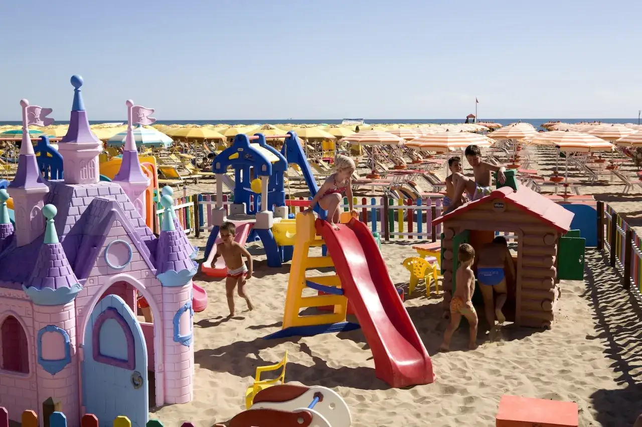 Bambini giocano in un'area giochi sulla spiaggia di Rimini, tra castelli e scivoli colorati. Un'idea perfetta per cosa fare a Rimini con i bambini!