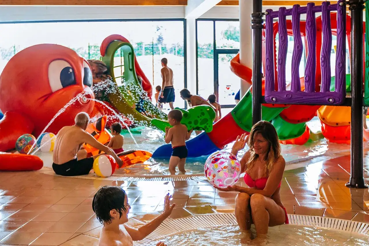 Bambini e adulti si divertono nelle terme per bambini con scivoli colorati e una grande attrazione a forma di polpo che spruzza acqua.