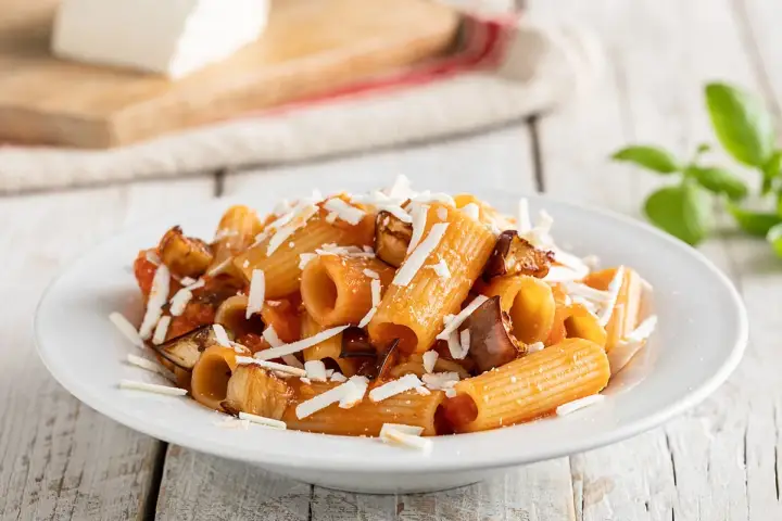 Un piatto invitante di pasta alla norma con melanzane fritte, pomodoro e ricotta salata grattugiata, pronto per essere gustato.
