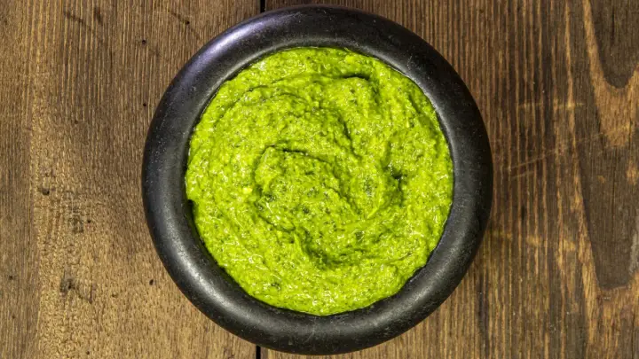 Pestello in pietra con un vibrante pesto alla genovese, pronto per condire la pasta.