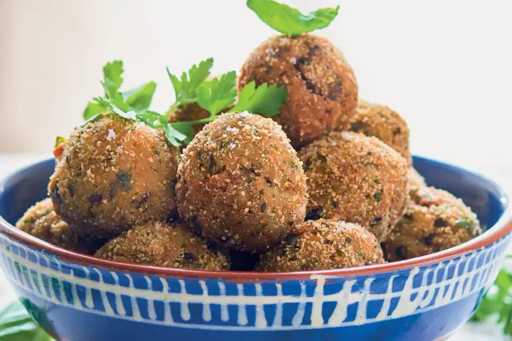 Polpette di melanzane dorate e croccanti, guarnite con prezzemolo fresco, in una ciotola blu decorata.