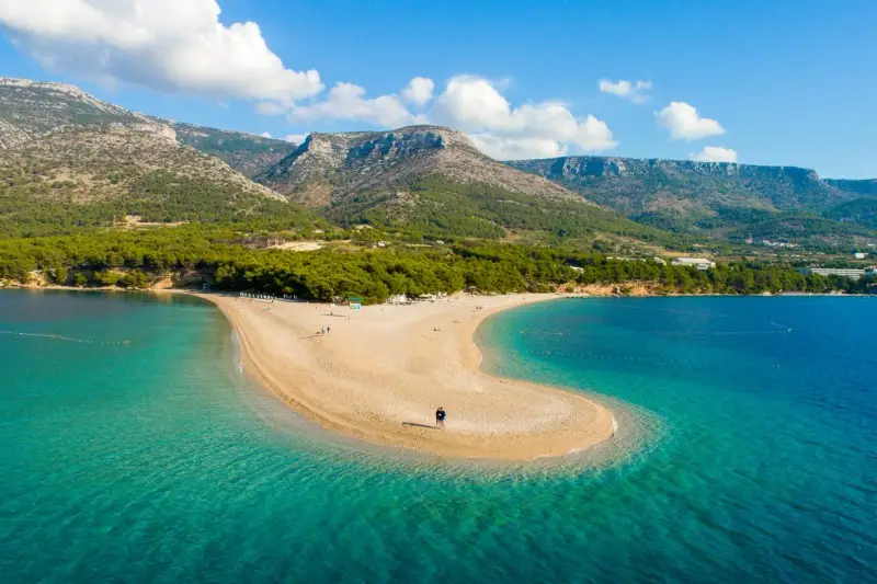 Spiaggia a forma di lingua di sabbia dorata, bagnata da acque cristalline, con montagne verdi sullo sfondo. Un angolo di paradiso in **Croazia mare**.